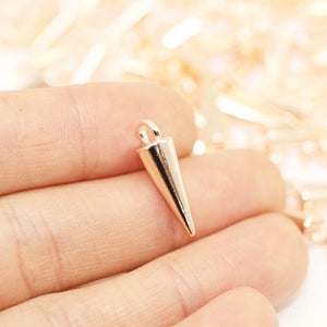 May include: A gold-toned metal cone charm with a loop at the top. The charm is approximately 2.5 cm long and is ideal for adding a touch of edgy style to jewellery projects.