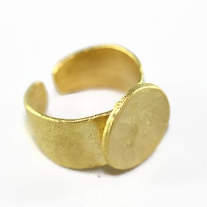 May include: A gold adjustable ring with a round, flat, blank surface. The ring is made of metal and has a smooth, polished finish.
