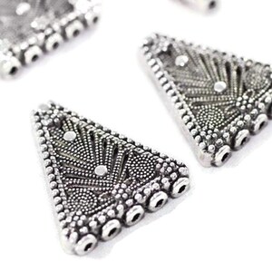 May include: Silver triangle-shaped pendant with a decorative design and multiple holes for stringing.