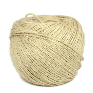 Puede incluir: Una bola de cuerda natural hecha de fibra de yute. La cuerda es de color beige claro y está enrollada en forma de bola.