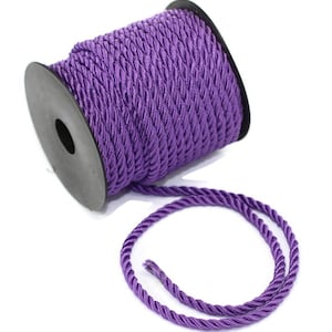 Könnte beinhalten: Eine Spule mit violetter, gedrehter Schnur. Die Schnur ist um eine schwarze Kunststoffspule gewickelt. Die Schnur ist etwa 6 mm dick.