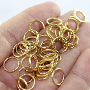 May include: A pile of gold jump rings, a type of jewelry finding, in a hand. The rings are small and round, and they are perfect for attaching charms, pendants, or other jewelry components.