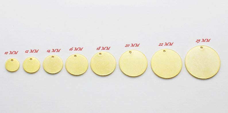 May include: A collection of brass-colored, round metal tags in various sizes, ranging from 10 mm to 25 mm in diameter. Each tag has a small hole at the top for attaching to a chain or other material. The tags are displayed on a white surface.