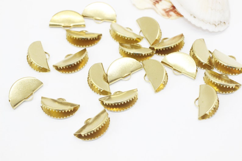 Może przedstawiać: Grupa złotych metalowych klamer w kształcie p&oacute;łksiężyca, niekt&oacute;re z falistym brzegiem, do tworzenia biżuterii.