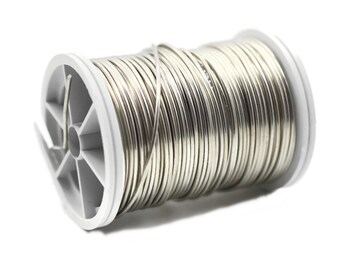 May include: A spool of silver wire on a white plastic spool. The wire is wound tightly around the spool.
