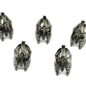 May include: Five silver-colored metal helmet charms with intricate details. The helmets are all facing forward and have a pointed top.