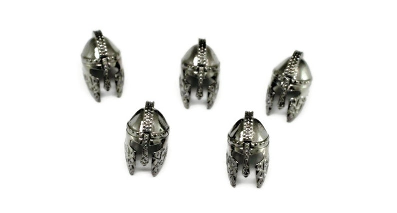 May include: Five silver-colored metal helmet charms with intricate details. The helmets are all facing forward and have a pointed top.
