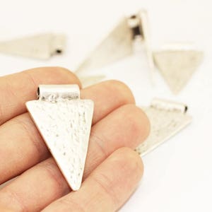 Könnte beinhalten: Ein Set mit sechs silbernen Dreiecksanhängern mit gehämmerter Textur. Die Anhänger haben oben eine Öse zum Anbringen an einer Kette oder Schnur.