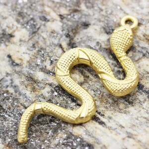 Peut inclure: Un pendentif en forme de serpent en or avec une surface texturée détaillée. Le charme est en forme de serpent avec la tête levée et une boucle en haut pour l'attacher à une chaîne ou un bracelet.