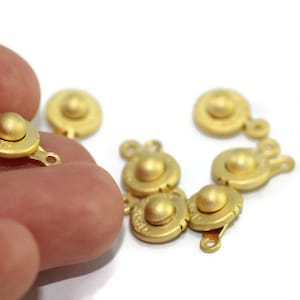 May include: A close-up of ten gold-toned metal clasps with a round, raised center. The clasps have two loops on each side.