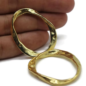 May include: Two gold-toned, hammered metal, open hoop earrings. The hoops are irregular in shape and have a slightly oval form.
