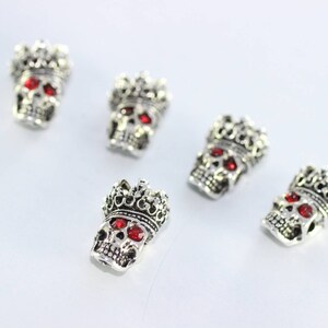 May include: Five silver skull charms with red gem eyes and a crown on top.