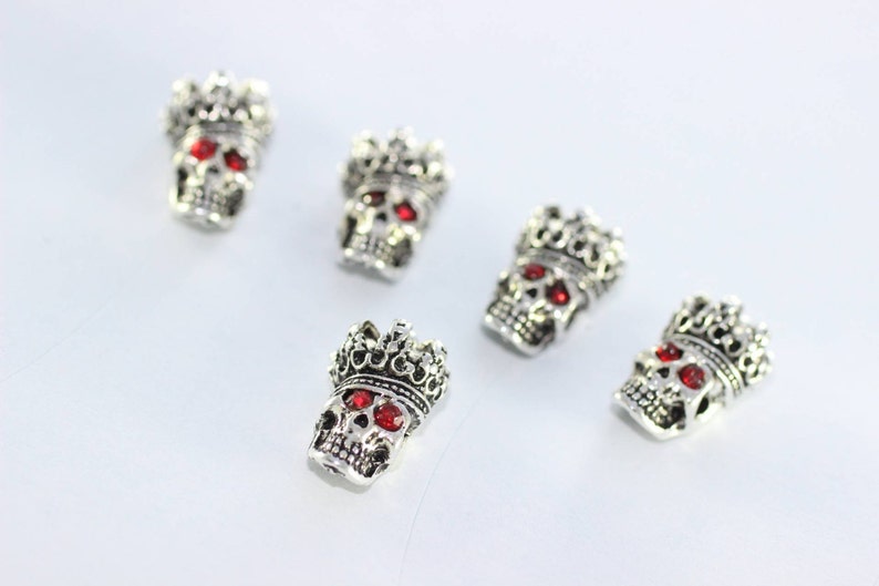 May include: Five silver skull charms with red gem eyes and a crown on top.