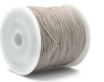 May include: A spool of light gray elastic cord, wound around a white plastic bobbin.