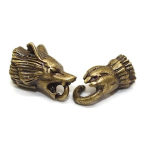 May include: Two antique gold-toned metal toggles, one shaped like a wolf's head and the other like a hand.