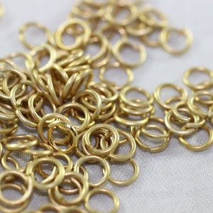 May include: A large pile of gold jump rings. The rings are small and round, and they are all linked together.