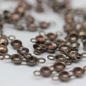 Peut inclure: Gros plan de nombreux capuchons de perles de couleur cuivre antique, chacun avec une petite boucle. Les capuchons de perles sont regroupés, certains étant nets et d'autres flous en arrière-plan. Ces composants sont parfaits pour la fabrication de bijoux et l'artisanat.