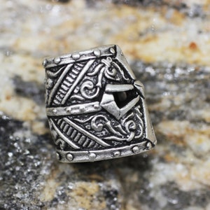 May include: Silver metal bead with a detailed design of a knight's helmet. The helmet has a visor and intricate carvings.