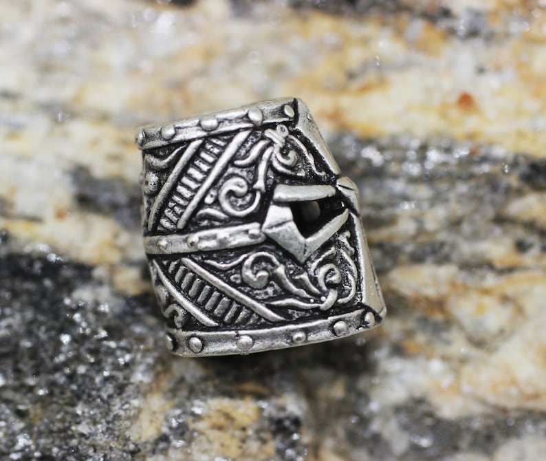 May include: Silver metal bead with a detailed design of a knight's helmet. The helmet has a visor and intricate carvings.