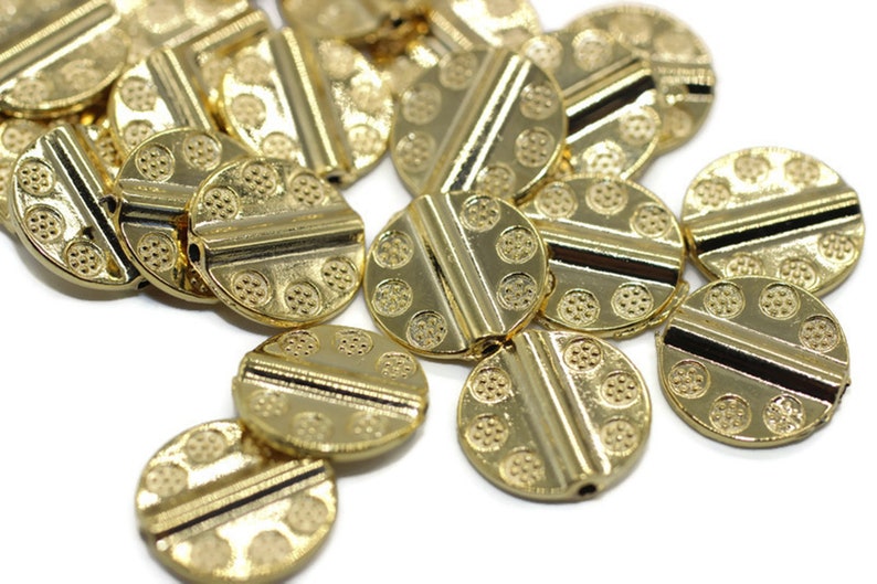 May include: A group of gold-colored metal beads with a decorative pattern. The beads are round and have a hole in the center for stringing.