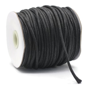 May include: A spool of black waxed cotton cord, wound around a white cardboard spool. The cord is approximately 1 mm thick and is ideal for jewelry making, macrame, and other crafts.