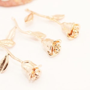 May include: Three gold-colored rose charms with stems and leaves. The roses are detailed and have a textured finish.