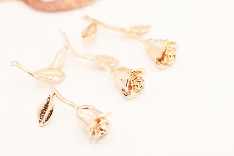 May include: Three gold-colored rose charms with stems and leaves. The roses are detailed and have a textured finish.