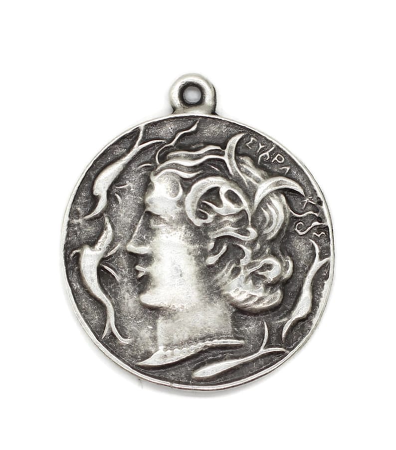May include: Silver pendant featuring a profile of a woman's face with flowing hair and intricate details. The pendant is circular and has the word "EYRPA" inscribed on the edge.