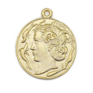 May include: Gold-toned metal pendant featuring a profile of a woman's face with intricate details. The pendant is circular and has a loop at the top for attaching to a chain.