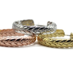 May include: Three hoop earrings in different metal finishes: rose gold, gold, and silver. Each earring has a braided design.