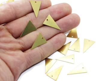 May include: A collection of gold-coloured triangle-shaped metal charms with a hole at the top. The charms are scattered on a white surface.