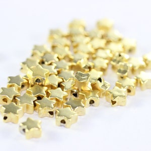May include: A pile of gold-colored star-shaped beads with a hole in the center of each star.