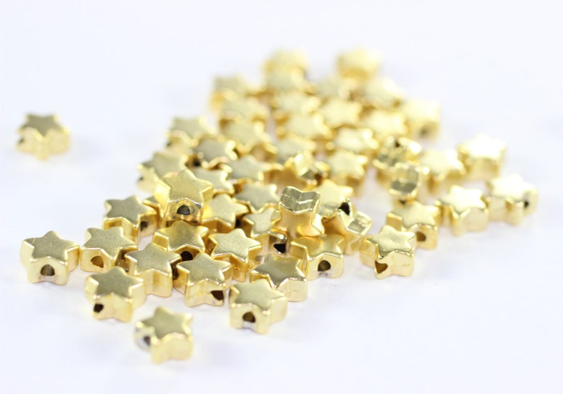 May include: A pile of gold-colored star-shaped beads with a hole in the center of each star.