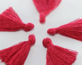 Könnte beinhalten: Fünf leuchtend rosa Stoffquasten mit einem geknüpften Oberteil. Die Quasten sind in einem Kreis auf weißem Hintergrund angeordnet.