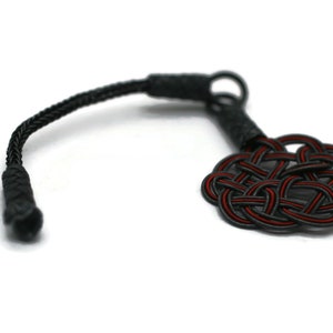 May include: A black cord with a red and black knotted charm. The knot is a complex design with multiple loops.
