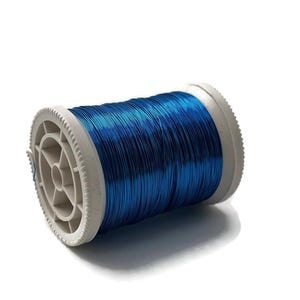 Puede incluir: Una bobina de alambre azul vibrante, enrollado firmemente alrededor de un núcleo de plástico blanco. El alambre tiene un brillo metálico, que refleja la luz. La bobina se encuentra sobre un fondo blanco limpio, resaltando el producto.