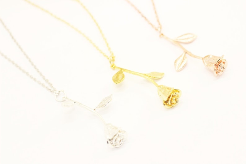 May include: Three gold rose necklaces with different colored finishes: silver, gold, and rose gold. The rose pendants are detailed and realistic.