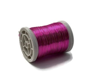 Könnte beinhalten: Eine Spule mit leuchtend magenta-farbenem Draht, eng auf eine graue Kunststoffspule gewickelt. Der Draht hat einen metallischen Glanz, der das Licht reflektiert. Dieses Bastelmaterial eignet sich für Schmuckherstellung, Perlenarbeiten oder andere kreative Projekte.