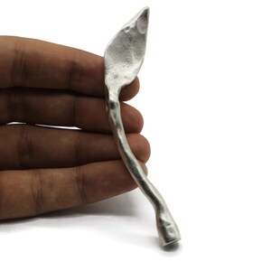 Może przedstawiać: Srebrna, abstrakcyjna rzeźba o organicznym kształcie, z ostrym zakończeniem i zaokrągloną podstawą.