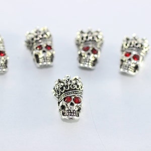 May include: Five silver skull charms with red rhinestone eyes and a crown on top.