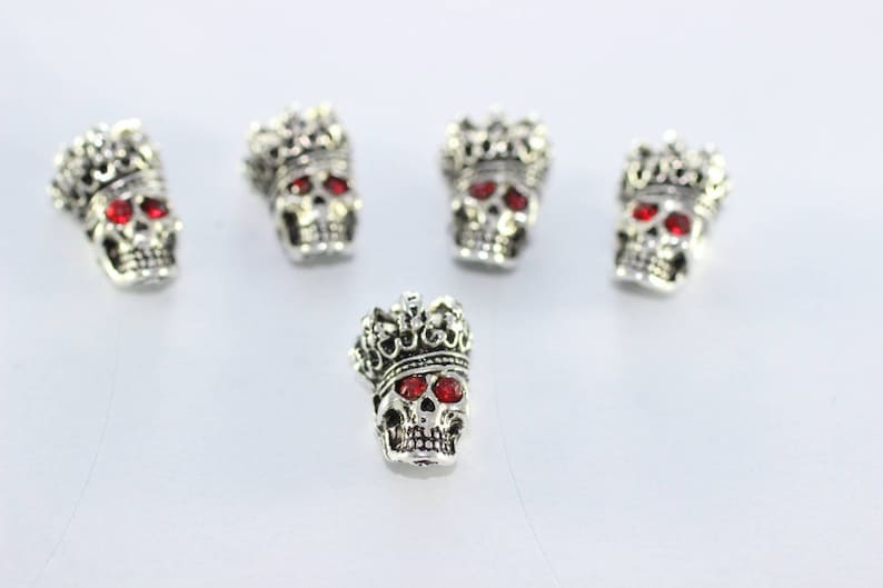 May include: Five silver skull charms with red rhinestone eyes and a crown on top.