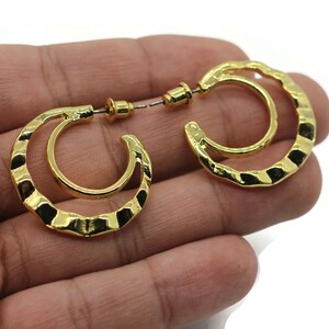 May include: A pair of gold-toned hoop earrings with a hammered texture. The earrings have a double hoop design.