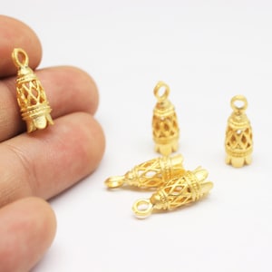 May include: Five gold-colored metal pendant charms in the shape of a bell with an intricate design. The charms have a loop at the top for attaching to a necklace or bracelet.