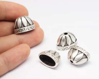 May include: Four silver metal decorative caps with a floral design. The caps have a small hole in the center and are designed to be used as end caps for cords or straps.