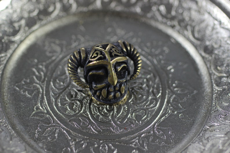 May include: A small, detailed, brass skull charm with horns and intricate designs. The skull is black with gold accents.