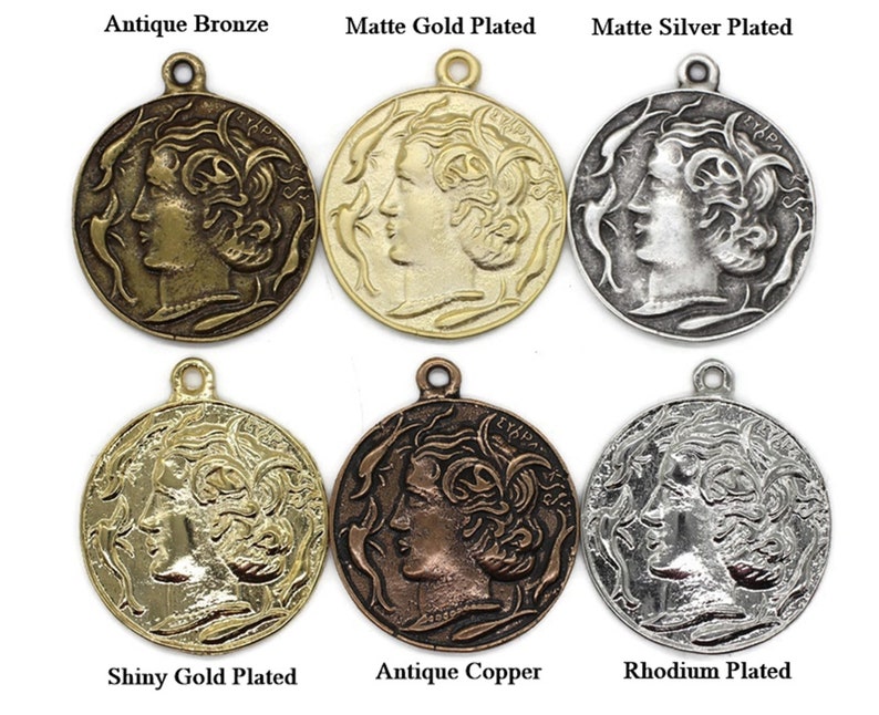 May include: Six round metal charms with a profile of a woman's face on each. The charms are in different finishes: antique bronze, matte gold plated, matte silver plated, shiny gold plated, antique copper, and rhodium plated.