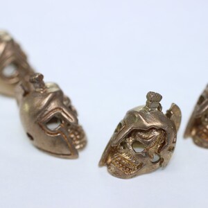 May include: Four small, detailed, gold-colored metal skull figurines with helmet-like features.