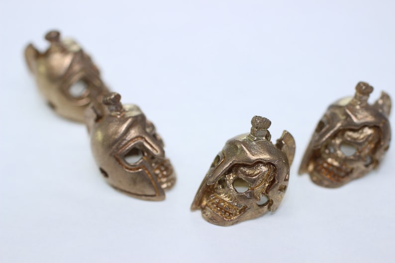 May include: Four small, detailed, gold-colored metal skull figurines with helmet-like features.