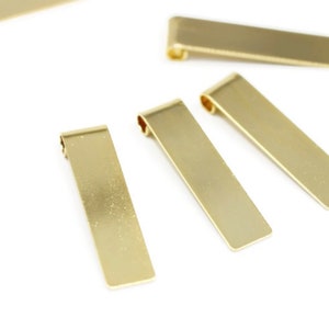 Peut inclure: Quatre étiquettes rectangulaires en métal de couleur dorée avec des coins arrondis. Les étiquettes ont un trou en haut pour être attachées à un collier ou un bracelet.