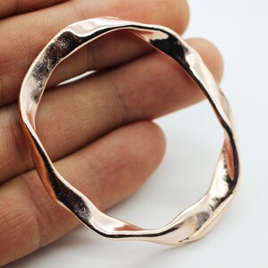 May include: A rose gold-colored metal ring with a wavy, irregular shape.
